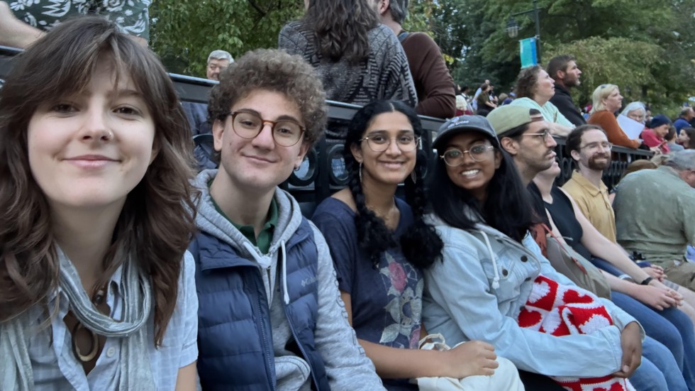Four students sitting on a bench outside near the Providence waterfront, smiling